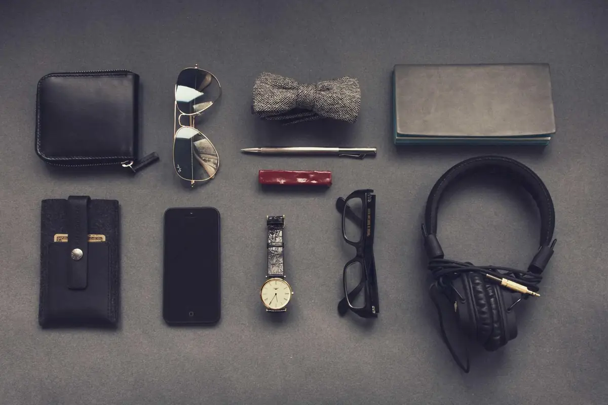 A wallet, sunglasses, a watch and headphones laid out on grey